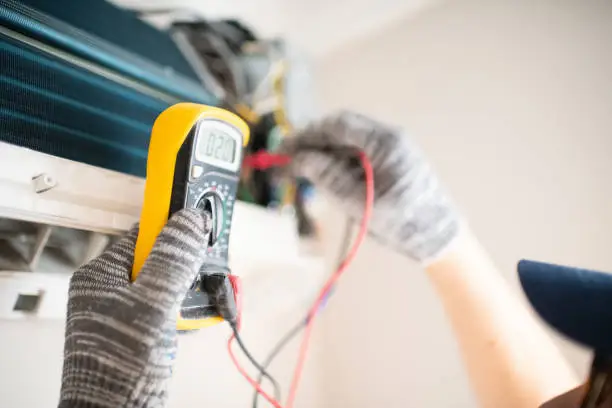 HVAC technician testing AC electrical components with diagnostic tools during repair visit