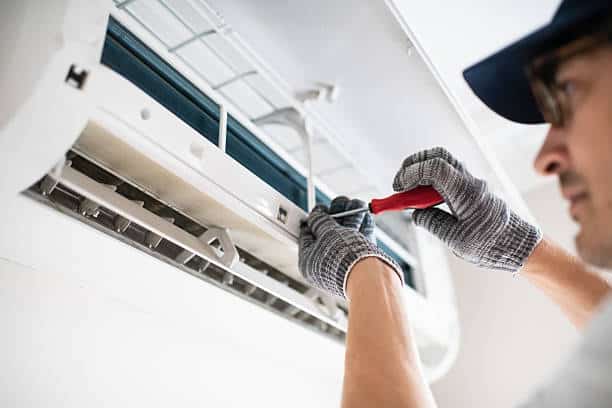 Technician repairing malfunctioning outdoor AC unit beside Long Branch coastal home